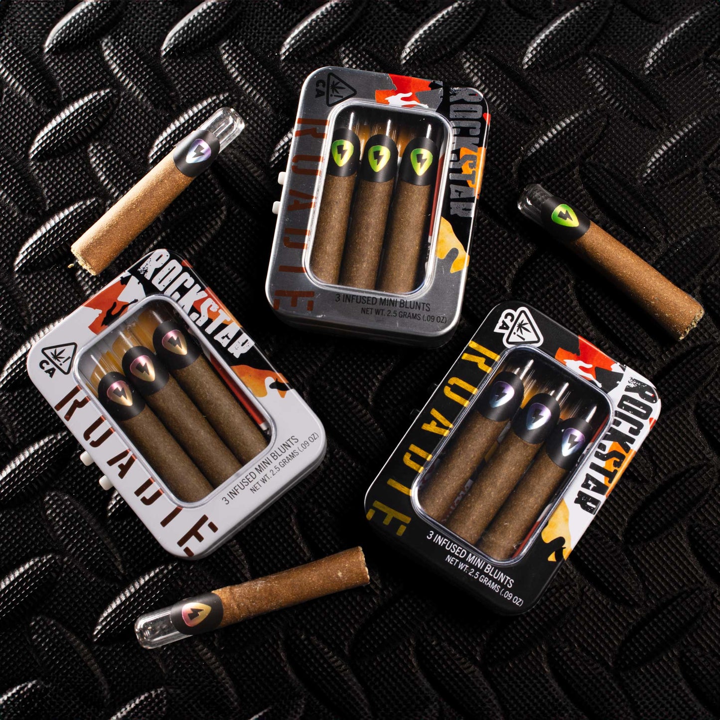 Flat lay of The Roadie infused blunts and tins on textured surface, showcasing 3-pack mini blunts with diamonds, hemp wraps, and glass tips.